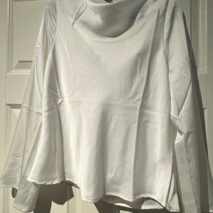 Vit draperad blus i satin, M - Säljer en vit draperad blus från GinaTricot i satinliknande material. Blusen har långa ärmar, lös passform och snygg drapering framtill samt knytband i nacken. Perfekt för dig som gillar stilrena och trendiga plagg med en lyxig känsla.