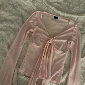 Ljusrosa långärmad omlottopp Gina Tricot - Supersöt ljusrosa långärmad topp från Gina Tricot med v-ringning och knyt framtill. Tunn och mjuk i materialet, perfekt för lager-på-lager eller som den är. Snygg omlottkänsla och figurnära passform som framhäver siluetten.