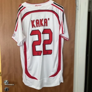AC Milan Kaka Champions League 2007 tröja - HELT OANVÄND AC Milan fotbollströja från Champions League-finalen 2007 i Aten, med Kaka och nummer 22 på ryggen. Vit med röda och svarta detaljer, broderat klubbmärke och Adidas-logga, samt Bwin sponsortryck. Tillverkad i polyester, kortärmad och med snygga kontrastpaneler.