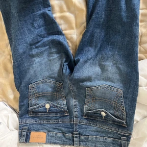 Blå jeans från Perfect Jeans - Snygga blå jeans från Perfect Jeans med slitningar på benen och coola bakfickor med lock och knapp. Jeansen har klassisk femficksdesign, raka ben och detaljerade sömmar. Perfekta för en avslappnad och trendig look.