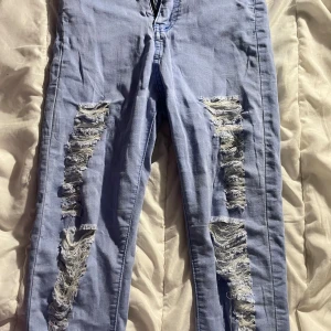 Ljusblå ripped skinny jeans, stl 27 - Ljusblå skinny jeans med slitna detaljer och stora ripped partier på båda benen. Klassisk femficksmodell med dragkedja och knapp. Snygg passform som sitter tight hela vägen ner. Perfekta för en avslappnad och trendig look.