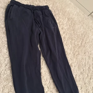 Mörkblå mjukisbyxor från Hugo Boss - Mörkblå mjukisbyxor från Hugo Boss med elastisk midja och snörning. Byxorna har sidofickor och diskret Boss-logga på ena benet. Perfekta för chill dagar eller när du vill ha en clean och avslappnad look.