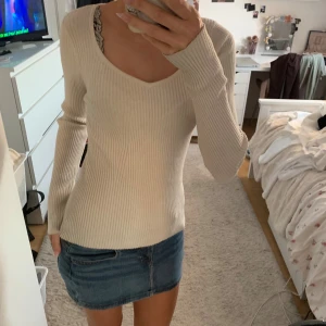 Ribbad beige långärmad tröja - Säljer en beige ribbad långärmad tröja med v-ringad hals. Tröjan har en slim passform och är tillverkad i ett mjukt stickat material som sitter snyggt på kroppen. Perfekt att styla med jeans eller kjol för en clean look.