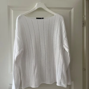 Vit stickad tröja med hålmönster - Vit stickad tröja med lång ärm och snyggt hålmönster i vertikala ränder. Tröjan har en loose passform och är perfekt för dig som gillar en enkel men ändå stilren look. Rund halsringning och mjukt material.