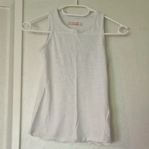 Vit linnetopp från Mywear Young - En basic vit linnetopp från Mywear Young i mjuk bomull. Toppen är ärmlös med rund halsringning och har en enkel, rak passform. Perfekt att matcha med jeans eller shorts för en clean look.