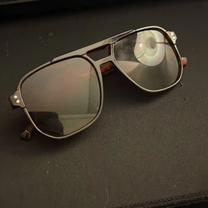 Svarta pilotbågar solglasögon - Snygga solglasögon med klassisk pilotform och svarta bågar. Glasen är mörka och ger en cool look, perfekt för att lyfta din stil. Metallbågar med dubbla nitar vid sidorna och detaljer vid näsryggen.