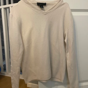 Beige kashmirtröja från Bloomingdale's - Säljer en stilren beige v-ringad tröja i 100% kashmir från Bloomingdale's The Men's Store. Tröjan har lång ärm, ribbade muddar och en klassisk passform. Perfekt för dig som gillar mjuka och lyxiga material.