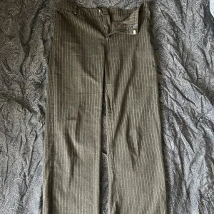 Gråa randiga kostymbyxor - Snygga grå kostymbyxor med tunna vita ränder. Byxorna har raka ben, bälteshällor och en bakficka. Klassisk passform och stilren look, perfekta för dig som gillar en clean och dressad vibe.