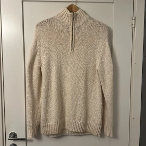 Gant stickad tröja - Säljer en beige stickad polotröja från GANT med half zip och ribbade muddar. Tröjan har hög krage och är långärmad, perfekt för kyliga dagar. Klassisk och stilren design med diskret GANT-logga på bröstet. Tröjan är i jättebra skick, säljes då jag aldrig använt den för den är för stor. Storlek S men passar även M.