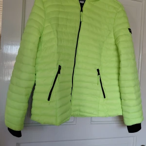 Neongul pufferjacka från Navahoo stl: XL - Säljer en riktigt snygg neongul pufferjacka från Navahoo. Jackan har huva, svarta dragkedjor och två fickor framtill. Den är quiltad och har en cool, sportig vibe som verkligen sticker ut. Perfekt för dig som vill synas och hålla dig varm under kyliga dagar. Stl: XL Mitt Pris: