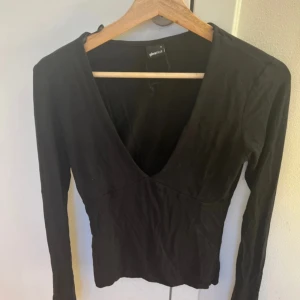 Svart v-ringad topp Gina Tricot - Svart långärmad topp från Gina Tricot med djup v-ringning. Toppens passform är figurnära och den är tillverkad i mjukt bomullsmaterial. Perfekt att styla med jeans eller kjol för en clean look.