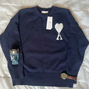 Ami Paris sweatshirt - Snygg mörkblå stickad tröja från Ami med rund halsringning och stor vit hjärtlogga med bokstaven A på bröstet. Tröjan har ribbade muddar vid ärmslut och nederkant, perfekt för dig som gillar stilrena och trendiga plagg.