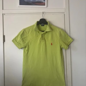 Limegrön Polo Ralph Lauren t-shirt S - Fräsch limegrön t-shirt från Polo Ralph Lauren i slim fit med klassisk krage och två knappar. Ikonisk röd broderad logga på bröstet. Tillverkad i 100% bomull för skön känsla. Perfekt för dig som gillar färg och stil.