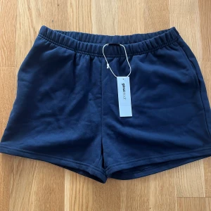 Mörkblå shorts från Gina Tricot - Säljer ett par mörkblå shorts från Gina Tricot med elastisk midja. De är tillverkade i mjuk bomull och har en enkel, klassisk design utan synliga detaljer. Perfekta för varma dagar eller chill hemma.