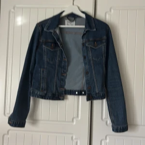 Blå jeansjacka från Pull&Bear - Klassisk blå jeansjacka från Pull&Bear med snygga bronsfärgade knappar och kontrastsömmar. Jackan har två bröstfickor med lock, sidfickor och justerbara knappar i midjan. Perfekt för dig som gillar en tidlös och avslappnad stil. Storleken är åt det mindre hållet.