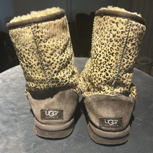 UGG boots med leopardmönster - Säljer ett par UGG boots med leopardmönstrad ovandel i beige och bruna toner. Skorna har mjukt foder och mockadetaljer vid hälen. Perfekta för dig som vill sticka ut med ett djurmönstrat statement på fötterna.