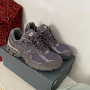 New Balance 2002R grå sneakers - Säljer ett par New Balance 2002R sneakers i olika nyanser av grått. Skorna har en snygg mix av mocka och mesh, med klassisk N-logga på sidan och robust sula. Perfekta för dig som gillar stilrena och bekväma sneakers med modern vibe.