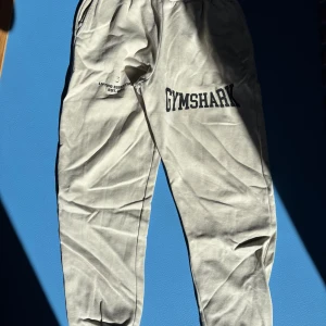 Beige mjukisbyxor från Gymshark XS - Beiga mjukisbyxor från Gymshark med svart tryck på benet och texten 'Lifting Essentials Est. 2012'. Byxorna har resår i midjan och är tillverkade i mjukt bomullsmaterial. Perfekta för chill eller gymmet. Passa till både kvinnor och men. Men är från kvinnoavdelningen! Använd 2-3 gågner då jag tycker dom är stora i storleken. Skulle sägga att detta är en S om inte M. Finns inte längre att köpa! Köpta för 500