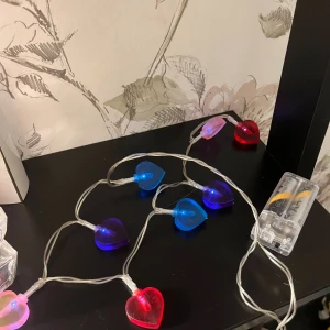 LED hjärtformad ljusslinga - Färgglad batteridriven LED-ljusslinga med hjärtformade lampor i blått, rött, lila och rosa. Perfekt för dekoration i hemmet eller till fest. Transparent kabel och batteridosa för två AA-batterier. Fungerar utmärkt, inga synliga defekter eller slitage.