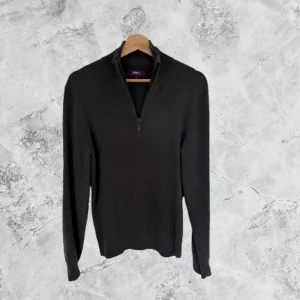 Mörkgrå halvzip tröja från Ströms - Snygg mörkgrå stickad tröja från Ströms med half zip och hög krage. Perfekt för dig som gillar stilrena plagg med enkel design. Långärmad och tillverkad i mjukt material som håller dig varm under kyliga dagar.