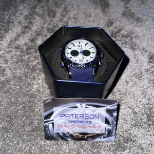 Paterson blå och vit sportklocka - Säljer en Paterson sportklocka med blått silikonarmband och vit urtavla. Klockan har svart vridbar ring, blå detaljer och tydliga siffror. Vattentät upp till 30 meter och har dual time-funktion. Kommer i originalförpackning med garanti.
