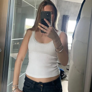 Vit ribbad linnetopp från Brandy Melville - Supersöt vit linnetopp med ribbad struktur och diskret hålmönster. Toppen har spetskant runt ringningen och axelbanden, vilket ger en romantisk vibe. Figurnära passform och croppad längd, perfekt till jeans eller kjol. Materialet känns mjukt och stretchigt.