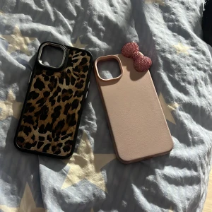 iPhone 13 Skal, Leopard & Rosa med Rosett - Två snygga iPhone 13 skal: ett med leopardmönster och svart ram, ett rosa med dekorativ rosett. Båda i fint skick utan synliga skador. Perfekt för att skydda och ge din mobil en personlig touch. Båda för 215