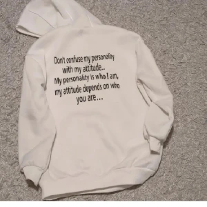 Vit hoodie med texttryck - Vit hoodie med huva och snörning. På ryggen finns ett svart texttryck: 'Don't confuse my personality with my attitude... My personality is who I am, my attitude depends on who you are...'. Mjuk och skön, perfekt för chill dagar.