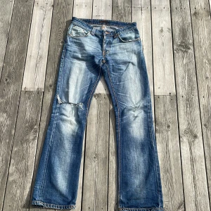 Nudie jeans - Snygga blå jeans från Nudie med snygg passform och slitningar. Jeansen har klassiska fem fickor, ljusa tvättade partier och råa kanter vid bensluten. Materialet är robust denim med coola detaljer på bakfickorna. Storlek 30 32. Pris kan diskuteras men då ska det vara raka rör. Fråga på.