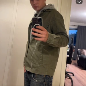 Olivgrön overshirt från H&M, M - Säljer en olivgrön overshirt från H&M i regular fit. Jackan har två bröstfickor med knappar, klassisk krage och knäppning framtill. Tillverkad i bomull och passar perfekt för lager-på-lager-stil. Enkel och clean design som funkar till det mesta.