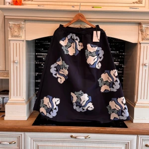 Blommig långkjol från By Malina - Snygg långkjol från By Malina med stora blommiga mönster i blått, vitt och grått på mörk botten. Kjolen har en A-linjeformad siluett och dragkedja bak. Perfekt för dig som vill sticka ut med en cool och trendig look.