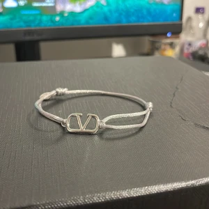 Valentino armband i silverfärg - Stilrent armband från Valentino med justerbart band i silverfärg och ikonisk V-logga i metall. Perfekt accessoar för att lyfta din outfit med en lyxig touch och minimalistisk design.