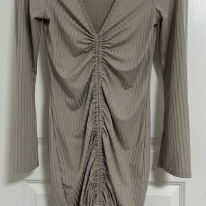 Beige ribbad omlottklänning - Säljer en beige kortklänning med ribbat tyg och snygg omlottdesign. Klänningen har lång ärm, v-ringning och cool rynkdetalj framtill som ger en trendig look. Perfekt för dig som gillar stilrena och moderna plagg.
