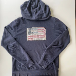  Ralph Lauren hoodie - Säljer en mörkblå hoodie från Ralph Lauren med en stor amerikansk flagga i vintage-stil på bröstet. Perfekt för dig som intresserad av en avslappnad stil👍