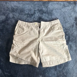 Beiga Peak Performance shorts - Säljer ett par beiga shorts från Peak Performance i klassisk modell med raka ben och praktiska fickor både fram och bak. De har bälteshällor och stängs med knapp och dragkedja. Perfekta för varma dagar och chill häng utomhus.