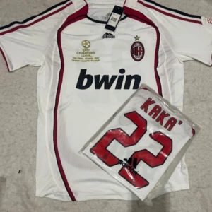 AC Milan Kaka Champions League tröja - AC Milan fotbollströja från Champions League-finalen 2007 med Kaka och nummer 22 på ryggen. Vit med röda och svarta detaljer, officiell Adidas med klubbmärke och Bwin-tryck på bröstet. Klassisk passform i lätt funktionsmaterial.