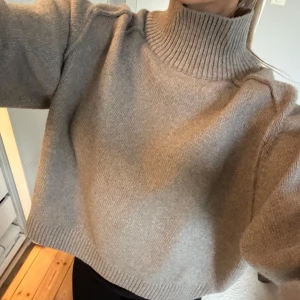 Beige stickad polotröja - Mysig beige stickad polotröja med bred ribbad krage och muddar. Tröjan har en loose passform och är perfekt för kyliga dagar. Enkel och stilren design som är lätt att matcha med olika outfits.