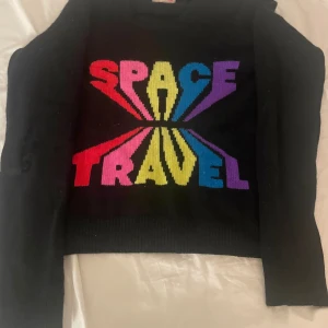 Svart stickad tröja From Future - Cool svart stickad tröja från From Future med färgglad SPACE TRAVEL-text i rött, rosa, gult, blått och lila framtill. Tröjan har lång ärm och ribbade muddar. Perfekt för dig som gillar statement-plagg och retro vibes. Storlek xs, det är ett hål på armen (kolla sista bilden för närbild)💖💕
