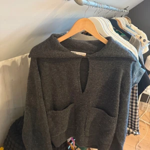 Mörkgrå stickad tröja från Zara - Mysig mörkgrå stickad tröja från Zara med stor krage, två framfickor och en snygg öppning framtill vid halsen. Perfekt för lager-på-lager och chill dagar. Tröjan har lång ärm och en loose fit som ger en avslappnad vibe.
