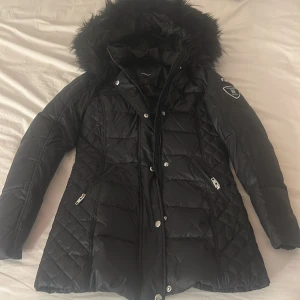 Svart Rockandblue beam mid jacket med päls - Skitsnygg svart dunjacka från Rockandblue med fluffig luva. Jackan har dragkedjor på fickor och ärm, Rockandblue-logga på ena ärmen. Perfekt för kalla dagar och har en stilren look och har ej fläckar/skador. orginalpriset var 3500, storlek 32 och den e ej använd💕💕