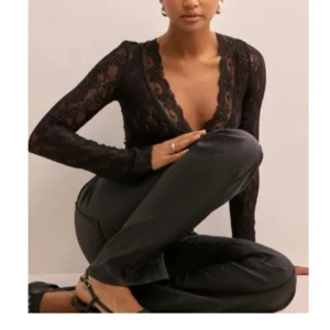 Svart spetsblus med djup v-ringning - Säljer en svart långärmad blus i spets med djup v-ringning och transparenta ärmar. Blusen har en feminin och elegant look med fina spetsdetaljer och figurnära passform. Perfekt för dig som vill sticka ut lite extra.