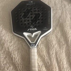 Stiga Cybershape 18K Padelracket - Stiga Cybershape 18K padelracket med 18K kolfiber och unik form för precision. Racketen har tydliga skador och sprickor på ramen, men greppet ser fräscht ut. Perfekt för dig som vill testa en toppmodell till ett lägre pris trots kosmetiska defekter. Nypris 3300kr