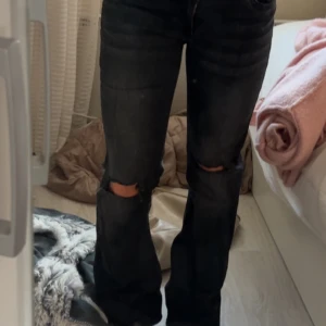 nelly jeans - Snygga svarta bootcut jeans från Nelly med slitna hål på båda knäna. Jeansen har klassisk femficksdesign och coolt broderad bakficka. Perfekt för dig som gillar en edgy och trendig look.