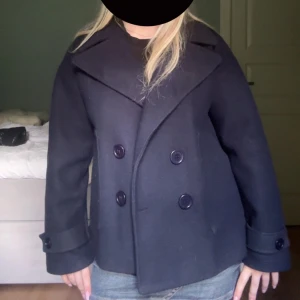 mörkblå Design by si kappa coat - Säljer en snygg mörkblå kappa med dubbelknäppning och breda slag. Jackan hae inga större tecken på användning och har använts sparsamt.