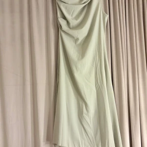 Ljusgrön långklänning med drapering - Säljer en elegant ljusgrön långklänning med snygg draperad urringning framtill. Klänningen är ärmlös och har en mjuk, flowy passform som faller fint längs kroppen. Perfekt för dig som vill ha en stilren och modern look.