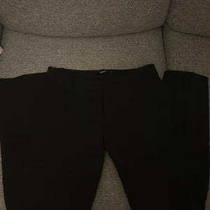 Svarta kostymbyxor från BikBok - Stilrena svarta kostymbyxor från BikBok i storlek 34. Byxorna har klassisk rak passform med hällor i midjan och dold knäppning framtill. Perfekta för en clean och snygg look.