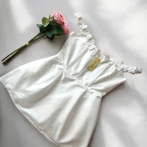 Klänning - Supersöt vit kort klänning från Lace & Beads med axelband dekorerade med små rosetter. Klänningen har en lätt utsvängd kjol och markerad midja. Materialet är glansigt och känns lyxigt, perfekt för sommarens alla tillfällen. Storlek 14. Skulle säga att den är en storlek L