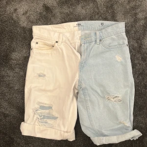 Tvåfärgade jeansshorts från FSBN XS - Unika jeansshorts från FSBN i storlek XS med cool tvåfärgad design – ena sidan ljusblå denim och andra sidan vit. Shorts med upprullade benslut och slitna detaljer med hål på båda sidor. Klassisk femficksmodell och bälteshällor. Perfekt för dig som vill sticka ut.