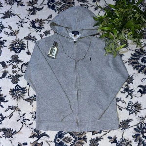 Grå hoodie från Polo Ralph Lauren XL - Snygg grå hoodie från Polo Ralph Lauren i storlek XL. Klassisk design med dragkedja, huva och två fickor framtill. Broderad logga på bröstet och mjukt material som känns skönt mot huden. Perfekt för chill dagar eller när du vill ha en clean look.