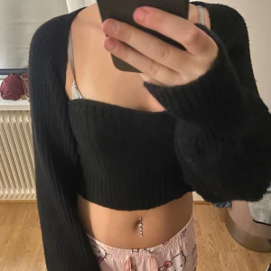 Svart croppad stickad topp - Säljer en svart croppad stickad topp med lång ärm löst till och fyrkantig urringning. Toppen är ribbad och har en tight passform över bröstet men är lite lösare i ärmarna. Perfekt att styla med höga jeans eller kjol för en trendig look. Köpte för 200 kr och inte använt mycket därför priset är 95